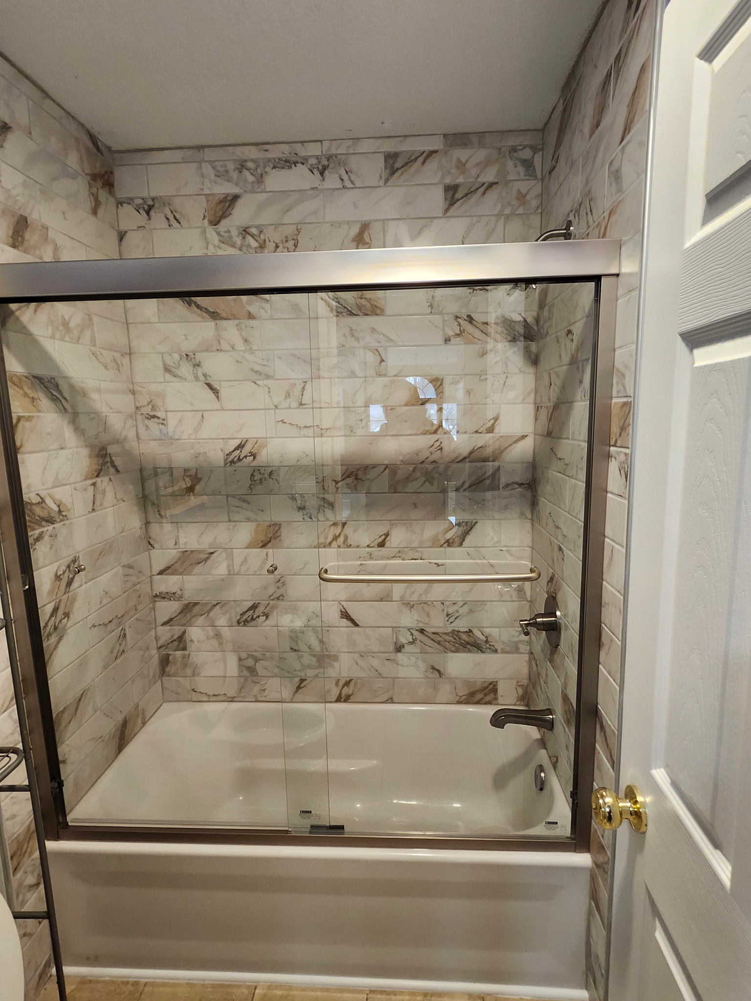 Bathtub with sliding glass doors, marble-look tile surround, and chrome fixtures