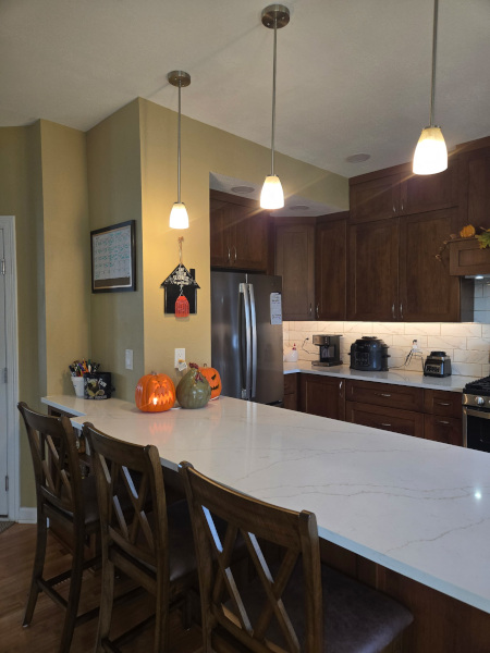 Kitchen island with white countertop, pendant lighting, bar seating, and dark wood cabinets