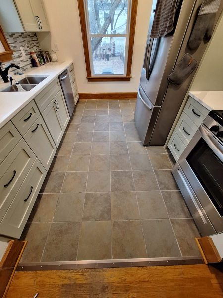 Modern galley kitchen with gray cabinets, stainless steel appliances, tiled floor, and a window