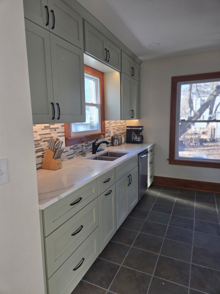 Kitchen with light green cabinets, white countertops, tiled backsplash, and window