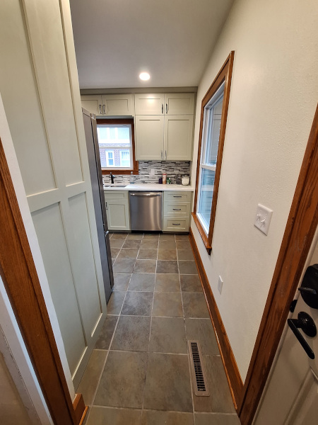 Galley kitchen with light cabinets, stainless steel dishwasher, tiled floor, and window